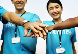 4 people in a circle wearing “volunteer” shirts putting their hands in the middle