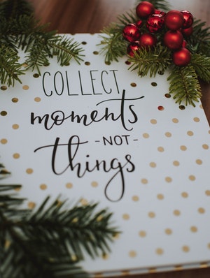 Photo of sign saying “Collect moments, not things” with evergreen and berries