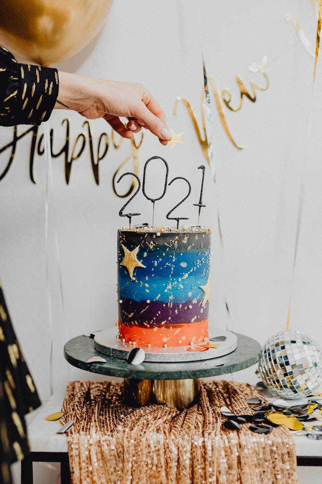 Hand holding gold star over a cylindrical cake with 2021 candles
