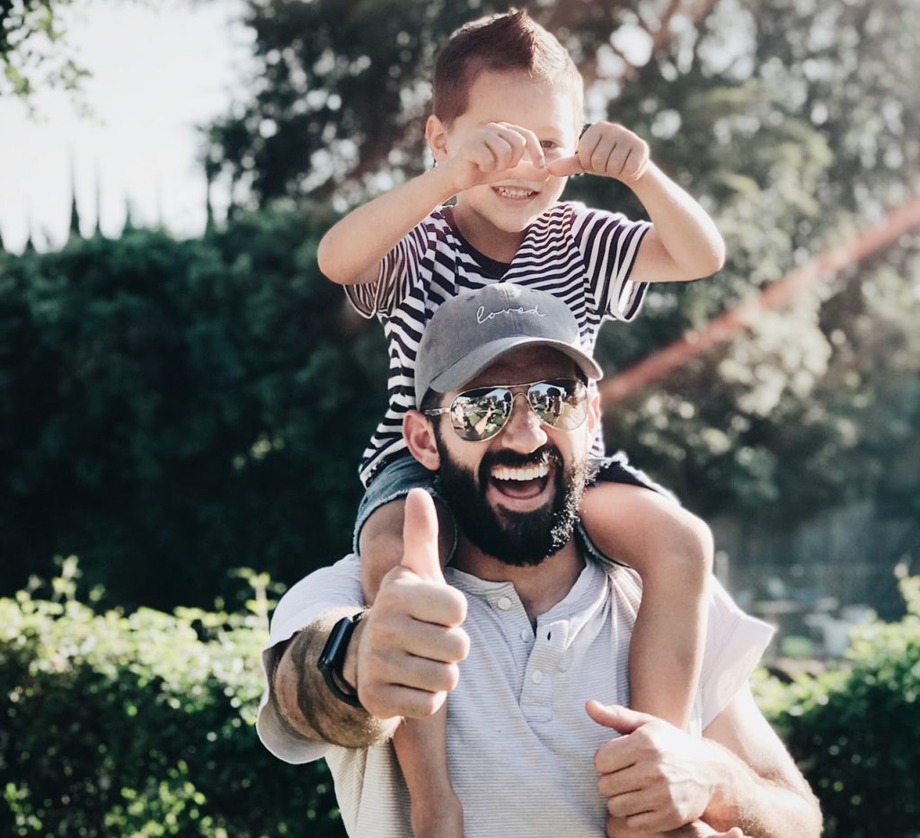 Smiling dad carrying happy kid on his shoulders on a sunny day